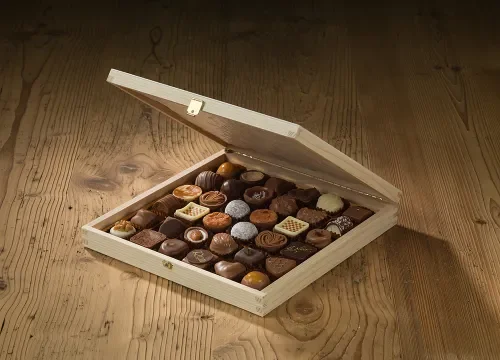 Pralinenkassette Klappdeckel mit einer Auswahl an handgefertigten Pralinen, sorgfältig arrangiert auf einem rustikalen Holztisch. Eine elegante Präsentation für edle Schokoladenspezialitäten.